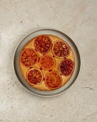 Cake with red oranges on beige marble background, flat lay