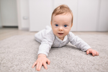 Charming newborn baby in a bodysuit lies on his stomach on a soft carpet. Happy baby lying on his stomach, textiles and bedding for children
