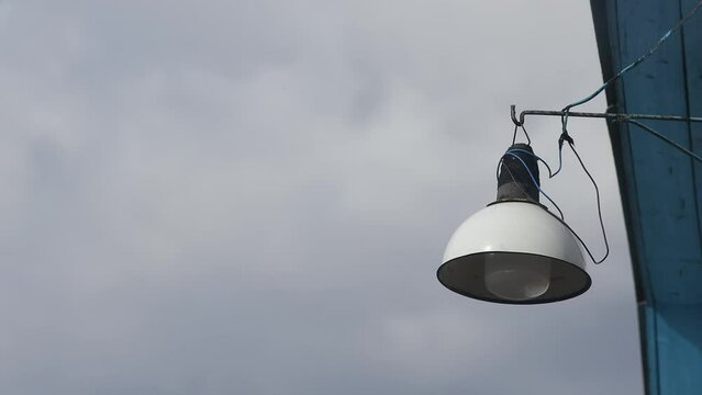 A lone shabby lantern dangles in the wind against a cloudy sky. High quality 4k footage
