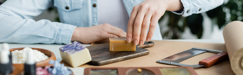 Fototapeta na wymiar Cropped view of craftswoman making soap on cutting board near supplies, banner.