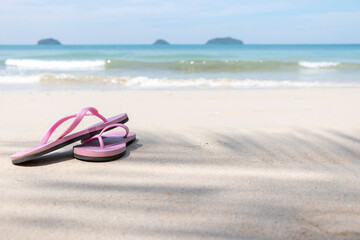 Beach flip-flops on the sand with a blurry view of the sea. Free space. Summer holidays.