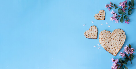 Banner. Layout of Traditional Matzah prepared for Passover with Matzah shape of hearts and pink flowers on blue background. top view. Spring Holiday of Jewish people. Fasting time