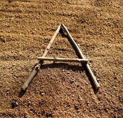 Letter A from small wooden sticks. Capital letter on sandy background. Wooden alphabet.