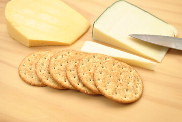 Wheat Crackers on a Wooden Cutting Board with Gourmet Cheeses and a Knife in the Background