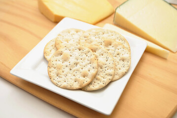 Sesame Crackers on a Wooden Cutting Board with Gourmet Cheeses and a Knife in the Background