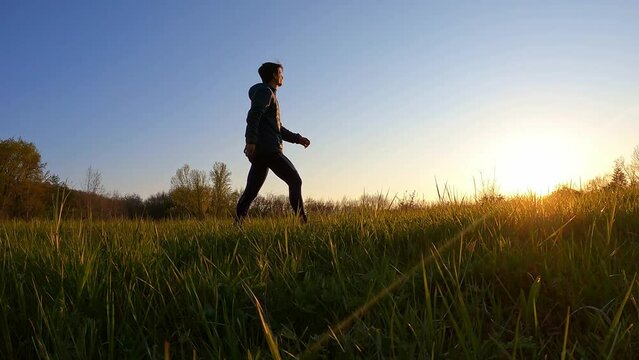 Jeune homme marchant dans un champ au cr&eacute;puscule. Randonn&eacute;e dans les derni&egrave;res lueurs du soir.