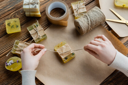 Top view of craftswoman holding twine near craft soap on paper at home.
