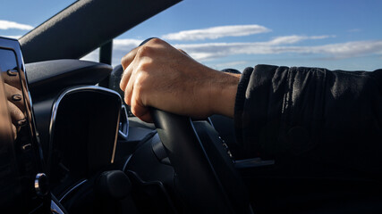 Close up of male hand holding steering wheel in the modern car at road trip.