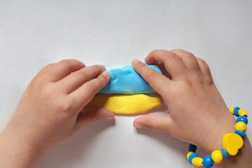 A child make the flag of Ukraine dough. Child with plasticine in the colors of the flag of Ukraine in hands. Children's creativity. DIY holiday handicraft and craft tools. Pray for Ukraine.