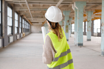 Female architect with blueprints in white helmet at construction site