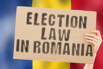 The phrase " Election law in Romania " on a banner in men's hands with a blurred Romanian flag in the background. Constitution. Political. Senate. Bucharest. Electorate. Majority