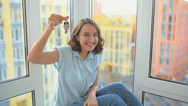 Relocation concept. Headshot of excited female moving in new home or apartment. Cheerful caucasian woman homeowner looking at camera and showing keys with keychain in her hand