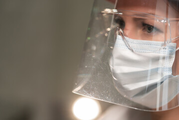 Young woman doctor or nurse working. Girl in medical mask, glasses and shield.