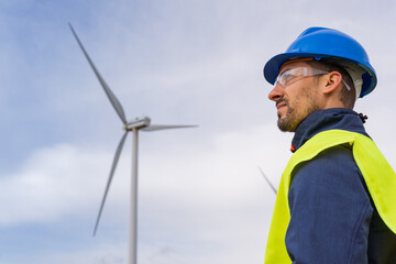 Renewable energy engineer looking at the sky with a wind power generator in the background. Maintenance operator with individual protection equipment in a wind farm. Leadership concept.