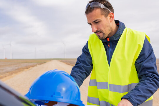 Energy Sector Worker Working On His Laptop In His Car At A Wind Farm. Renewable Energy, Clean Energy And Climate Change Concept.