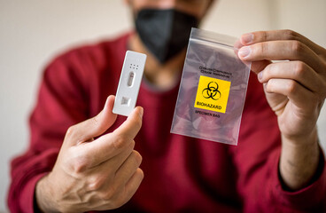 Quick Covid Virus Test with Negative Result and Clear Biohazard Bag Shown on Camera by Black Masked Man's Hands