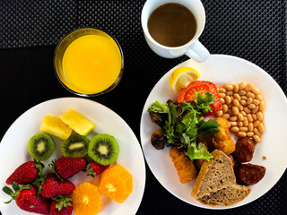 Breakfast time. Healthy breakfast. English breakfast. Berries and fruits, pastries, coffee on a black background. Fruit mix: ripe Strawberries, pieces of orange, kiwi and pineapple. Kind of English 