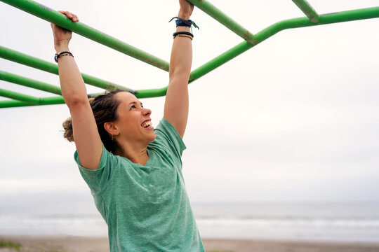 young woman doing excercise on hanging pull up bar outdoors on the beach