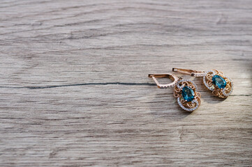 Diamond earrings on wooden background. Drop earrings with blue crystals, jewelry. Two golden...