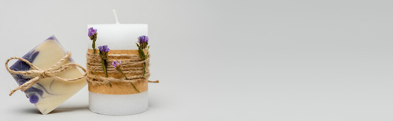 Craft candle with flowers near soap bar on grey background, banner.