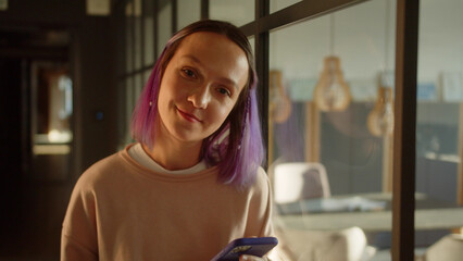 A young girl-student stands near the window, meets her friend and then reads posts on the Internet, smiling