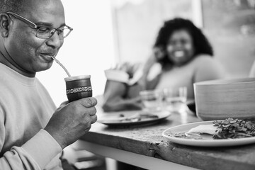 Happy black father drinking yerba mate during lunch at home - Main focus on cup - Black and white editing