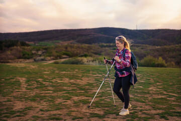 A mature woman in her 50s walks in the mountains. Use hiking poles.