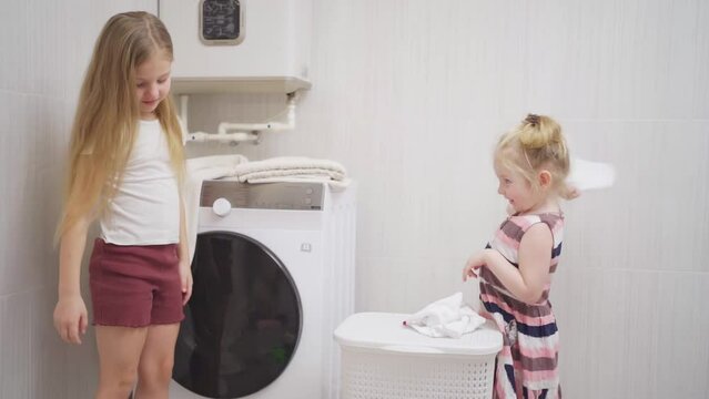 two cute and cheerful girls play with laundry in the laundry room. 