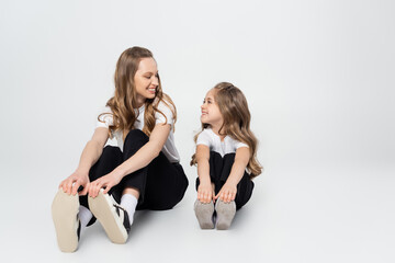 mother and daughter in black and white clothes smiling at each other while sitting on grey background.