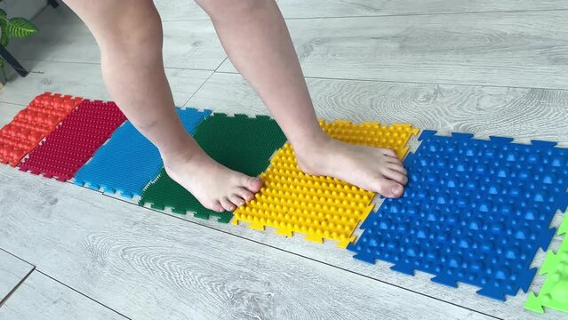 Little boy steps on orthopedic massage mats with different stiffness and texture. Feet Massage Using Trigger Point Spiky Massage Ball. Myofascial Release.