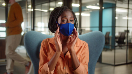 Sitting in the entrance hall in the university, a young african professor is talking about the importance of wearing a protective mask and putting it on her face, close up