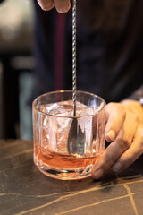 Preparation of a cocktail in a wide glass with whiskey and a large ice cube and citrus in a bar