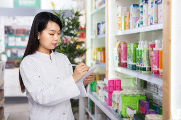 Chinese female is checking medicine with notebook in pharmacy