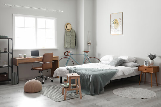 Interior of light room with bed, modern workplace and bicycle