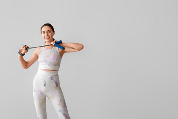Sporty young woman with skipping rope on grey background
