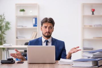 Fototapeta premium Young male employee unhappy with excessive work in the office