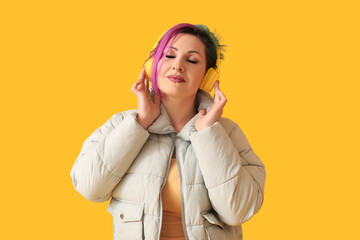 Beautiful woman with unusual hair listening to music on yellow background