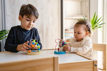 Brother and sister playing at home siblings children baby girl and five years old boy play with toys in bright room in day front view copy space family life concept growing up