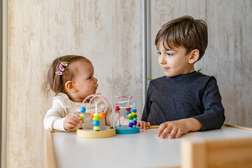Naklejka premium Brother and sister playing at home siblings children baby girl and five years old boy play with toys in bright room in day front view copy space family life concept growing up