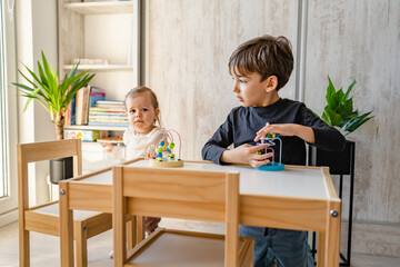 Brother and sister playing at home siblings children baby girl and five years old boy play with toys in bright room in day front view copy space family life concept growing up