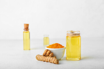 Bottle of oil, turmeric root and bowl with powder on light background