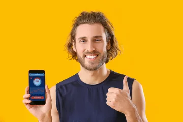 Foto op Plexiglas Sporty man holding phone with installed app for calories counting and showing thumb-up on color background © Pixel-Shot