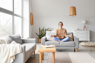 Beautiful young woman meditating on couch at home