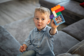 Fototapeta premium A small child plays with blocks. The boy sits on the sofa and builds a house from the constructor.