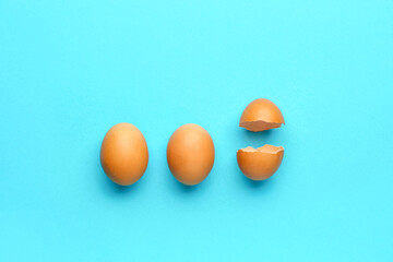 Cracked and whole chicken eggs on blue background