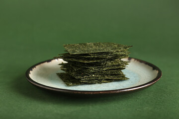 Plate with tasty seaweed sheets on green background © Pixel-Shot