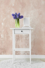 Vase with hyacinth flowers, book and blank photo frame on table near color wall in room