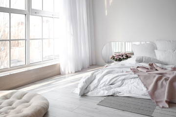 Comfortable bed and begonia flowers near white wall in room interior