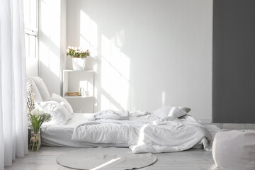Comfortable bed and beautiful flowers in light room interior
