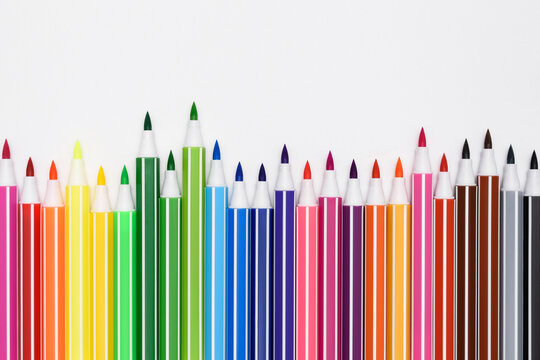 A set of bright multi-colored markers on a white paper background. Colorful children's felt-tip pens folded in a row at different heights. Close-up shot, cropped image.
